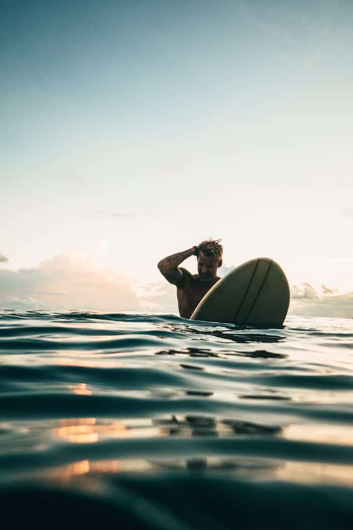 A surfer enjoys the serene waters and a stunning sunset on the coast of Indonesia, perfect for adventurers.
